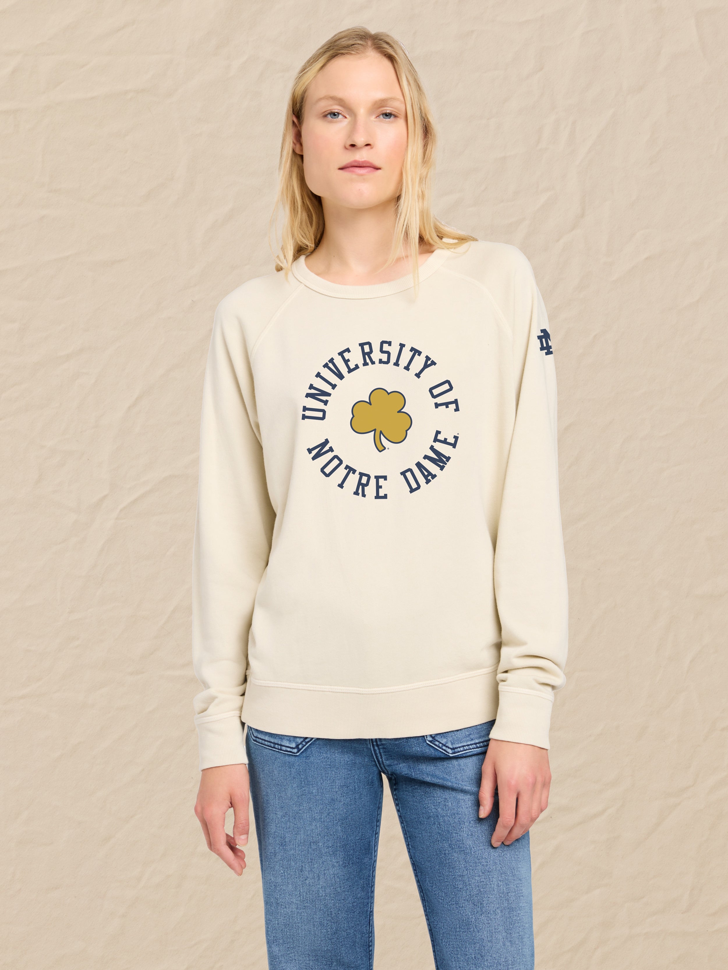 Woman wearing an ivory crewneck sweatshirt with Notre Dame graphic on the chest against a beige background