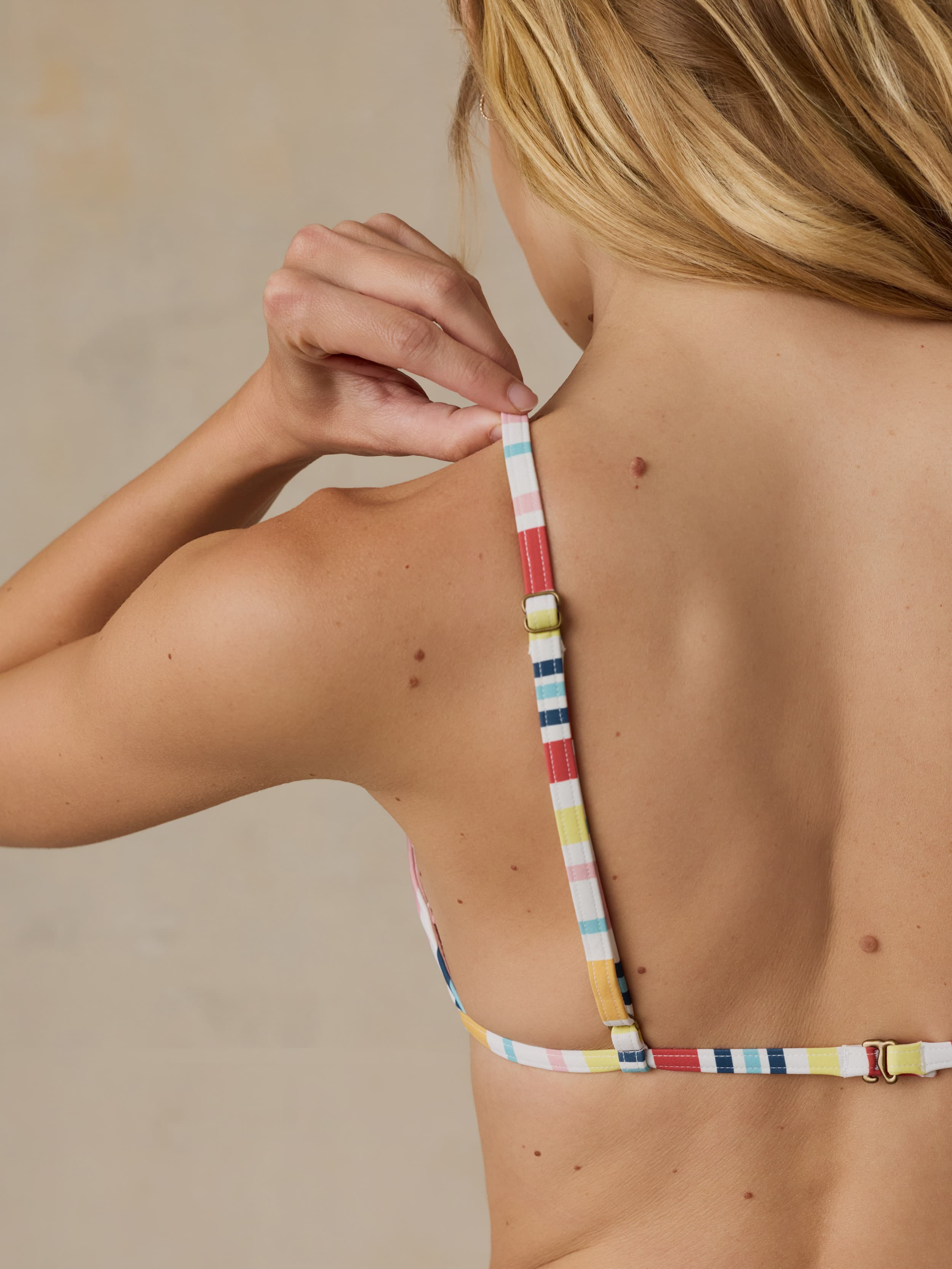 Woman wearing a colorful striped bikini top against a neutral background
