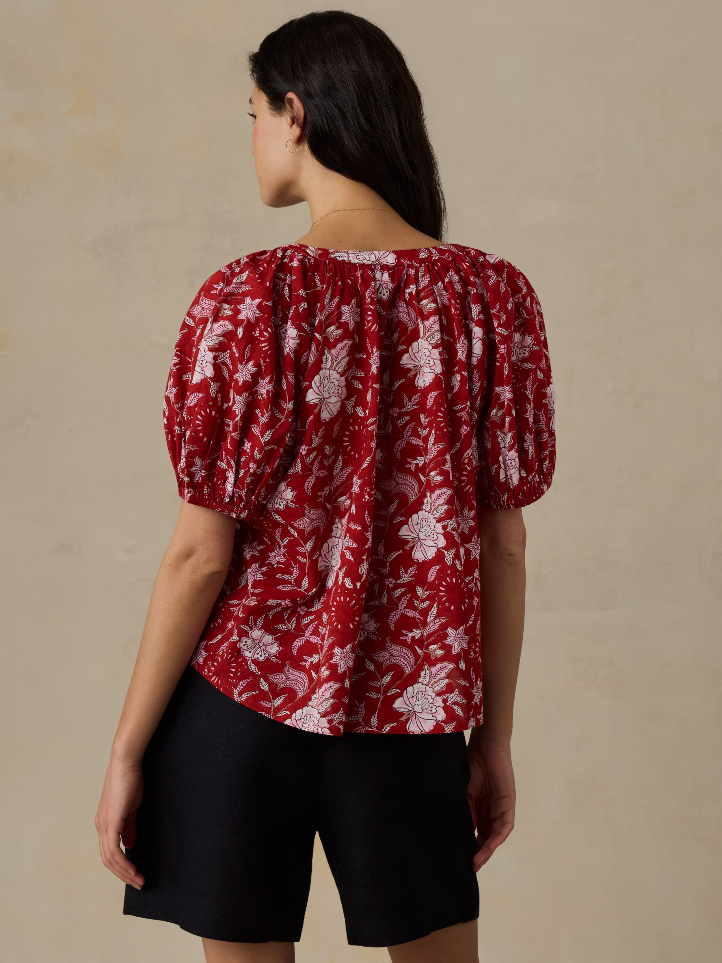 Woman wearing a red floral blouse with black shorts against a beige background