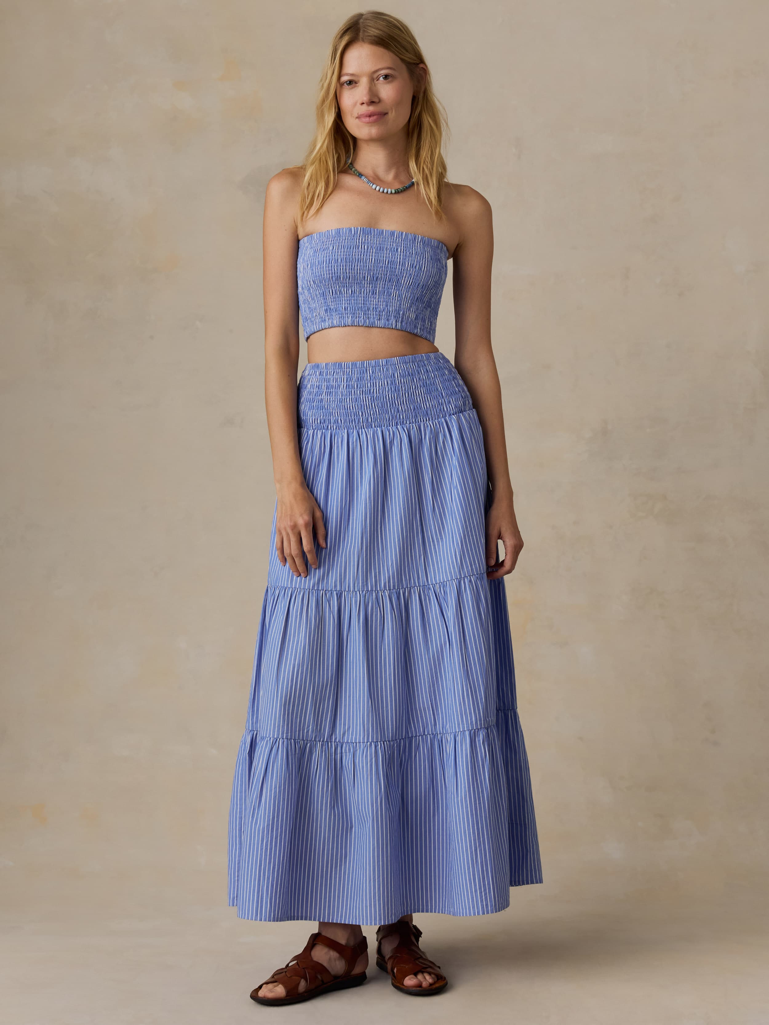 Woman wearing a blue strapless top and skirt set against a beige background