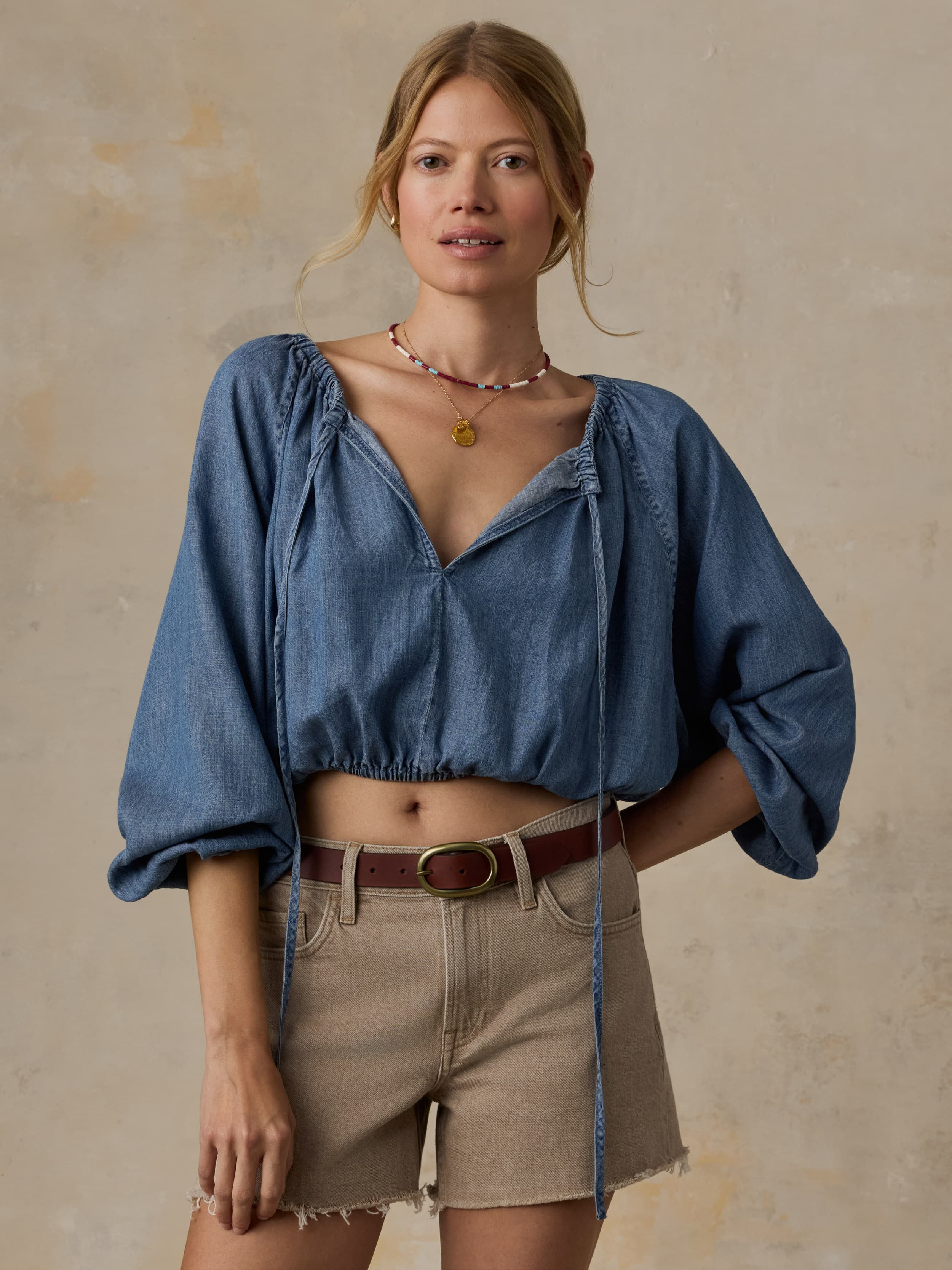 Woman wearing a blue denim top and beige shorts against a beige background