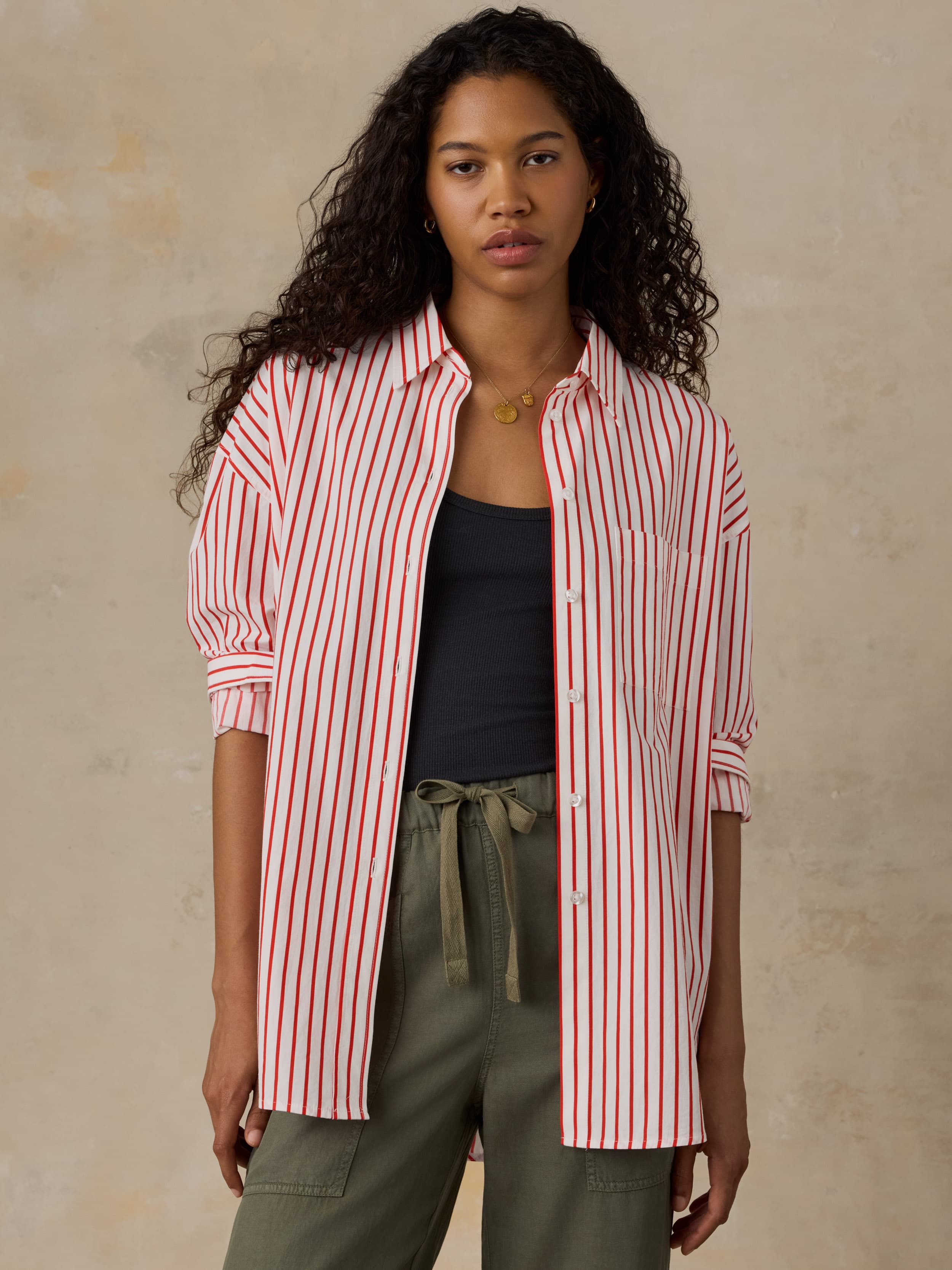 Woman wearing a red and white striped shirt over a black top and green pants on a beige background