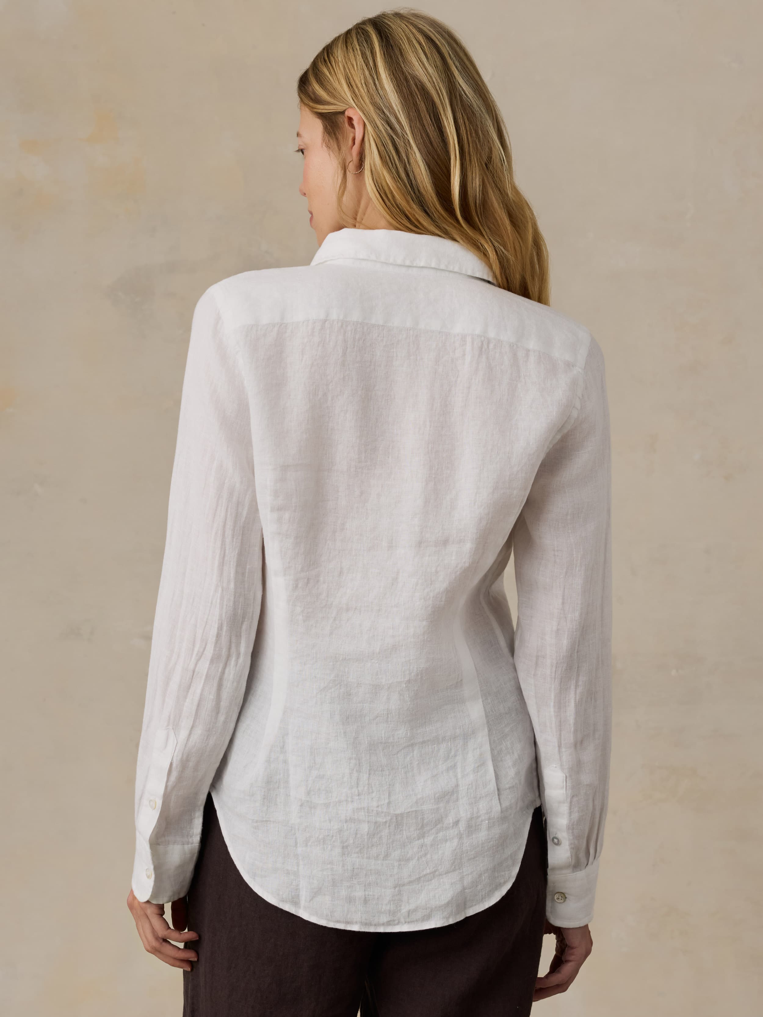 Woman wearing a white linen shirt and brown linen pants against a beige background
